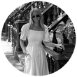 Black and white image of Sophie, copywriter, waering a white dress while leaning against a brownstone and smiling. 